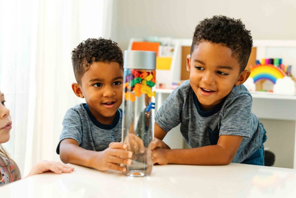 2 boys looking at a sensory bottle with alphabet beads