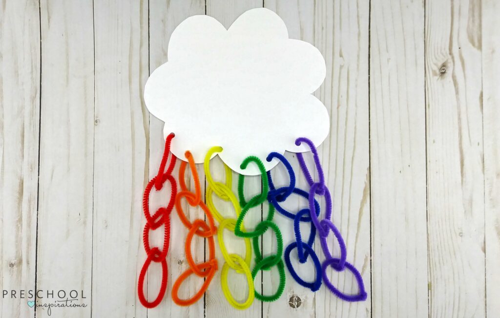 Pipe cleaner rainbow craft using rainbow colored pipe cleaners looped in circles through each other. Attached to a paper cloud through punched paper. 